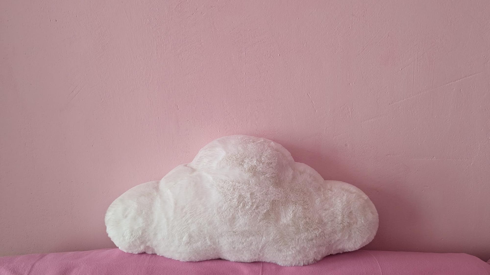 a cloud-shaped pillow on a pink couch before a pink wall.