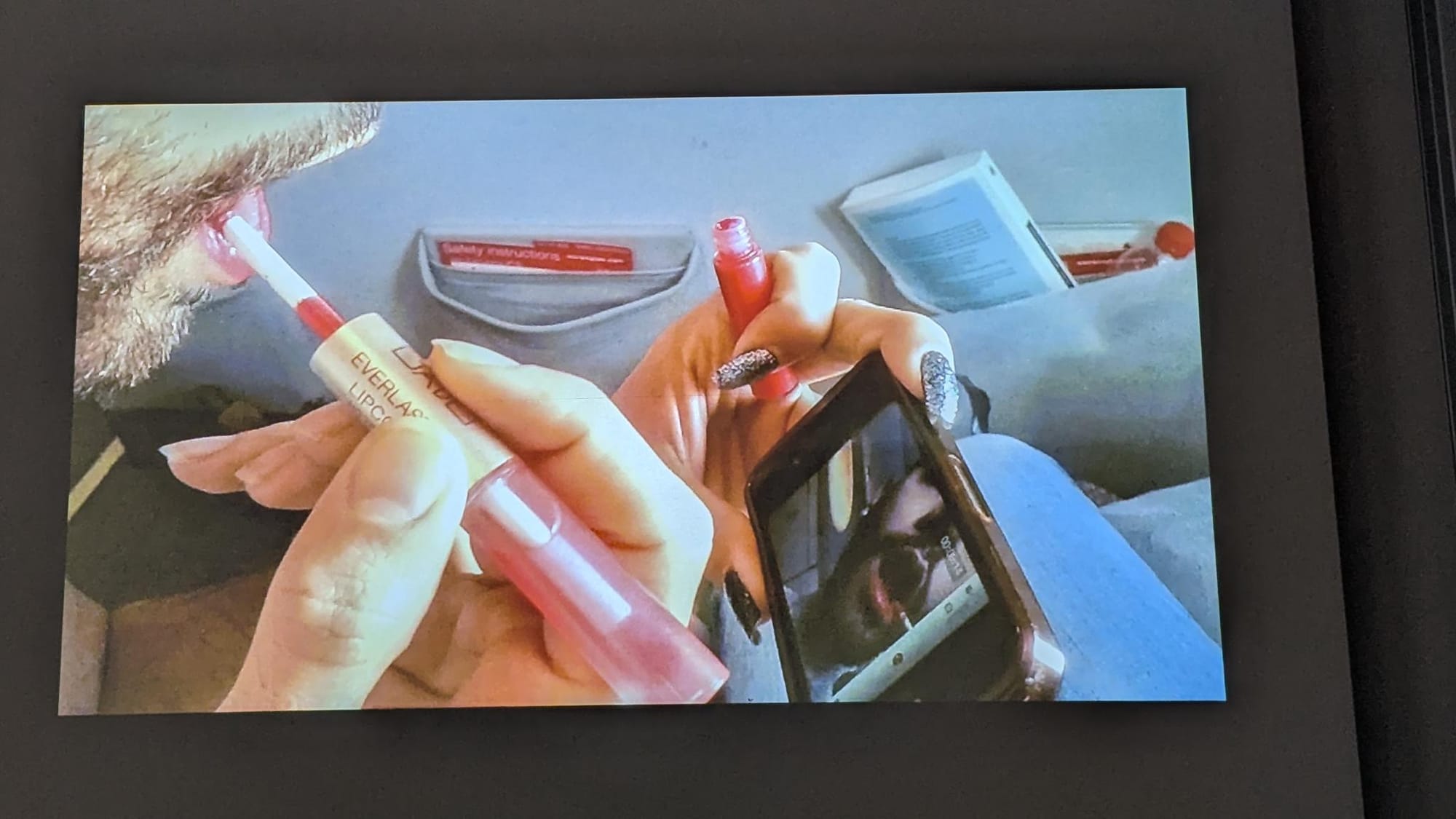 still from the short film "homecoming queenz" by oz marinov & elias wakeem (2012) showing one of them applying lipstick on an airplane.