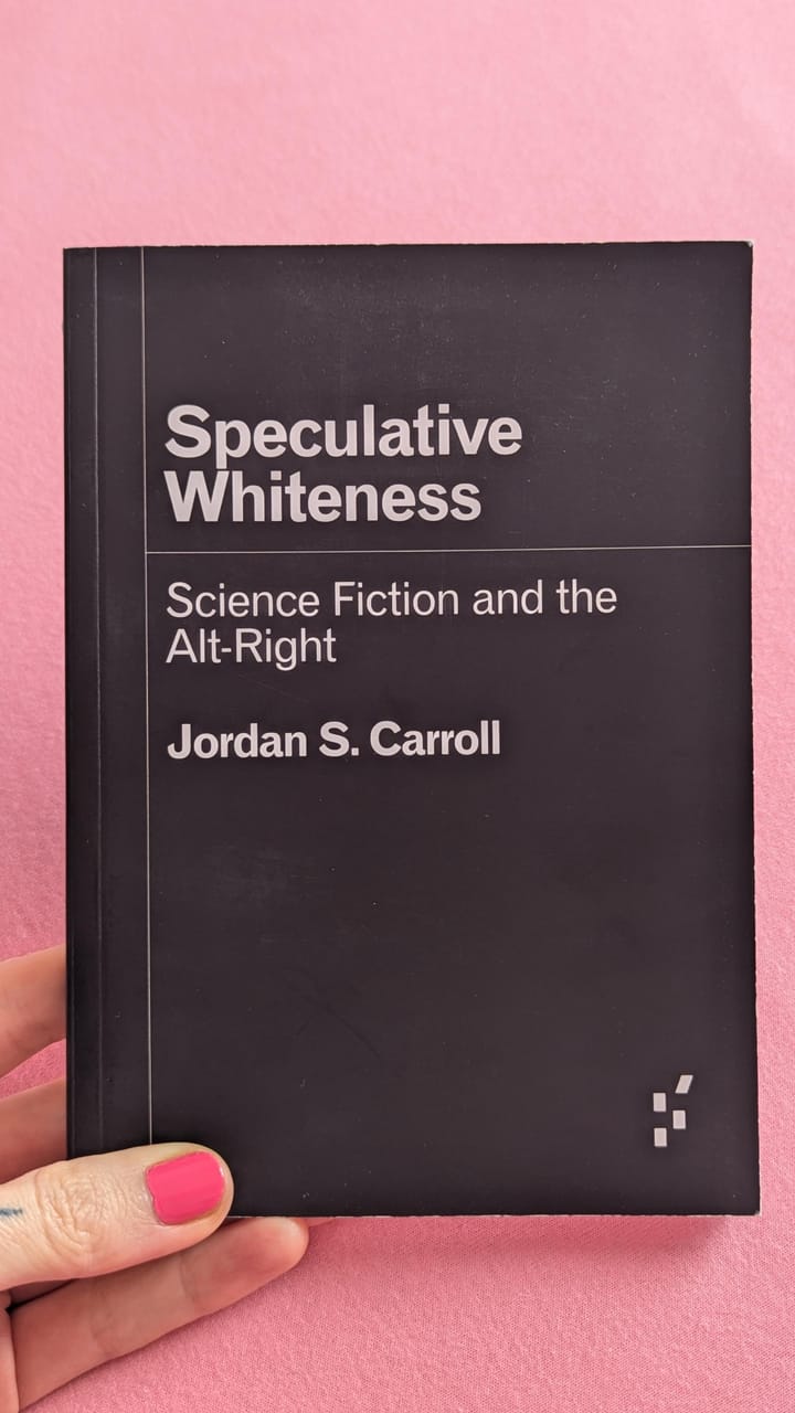 my hand holding a paperback copy of "Speculative Whiteness: Science Fiction and the Alt-Right" by Jordan S. Carroll